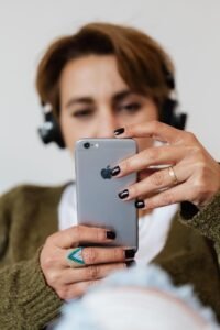 Blurred female in casual clothes wearing stylish ring surfing contemporary mobile phone and listening to music via headphones